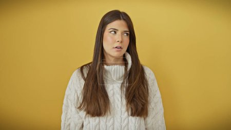 Hispanic young woman in white sweater over yellow background looking away thoughtfully.