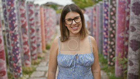 Cheerful hispanic woman in glasses poses with joy, smiling radiantly in kyoto's famous kimono forest, radiating pure happiness and casual confidence in a beautiful adult portrait.