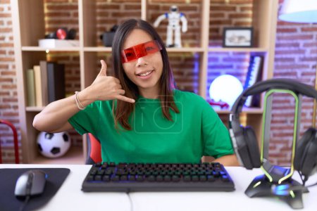 Foto de Mujer china de mediana edad con gafas de realidad virtual sonriendo haciendo gesto telefónico con la mano y los dedos como hablar por teléfono. comunicar conceptos. - Imagen libre de derechos