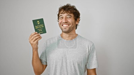 Téléchargez les photos : Jeune homme joyeux, tenant son passeport arabe saoudien, rayonnant avec confiance sur un fond blanc isolé, prêt à profiter de ses vacances de rêve! - en image libre de droit