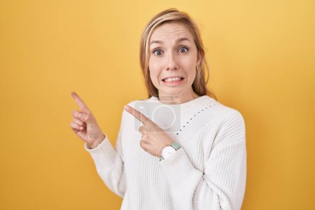 Photo for Young caucasian woman wearing white sweater over yellow background pointing aside worried and nervous with both hands, concerned and surprised expression - Royalty Free Image