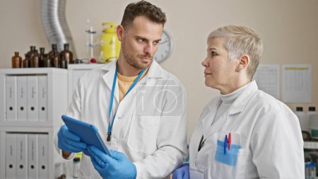 A man and a woman in lab coats discuss results on a tablet inside a laboratory, highlighting teamwork and medical research.