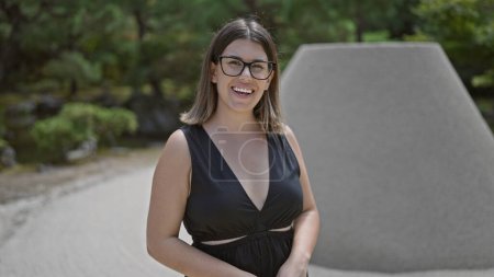 Photo for Joyful and confident, a beautiful hispanic woman in glasses stands by the serene ginkaku-ji temple, her cheerful smile embracing the beauty of kyoto's zen garden - Royalty Free Image
