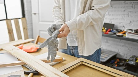 Foto de Un hombre que usa guantes en un taller manejando herramientas, y proyectos de carpintería que encarnan sutilmente la artesanía. - Imagen libre de derechos