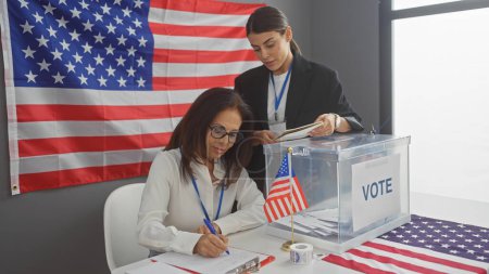 Foto de Dos mujeres trabajando en un centro electoral americano con boleta electoral y bandera de nosotros. - Imagen libre de derechos
