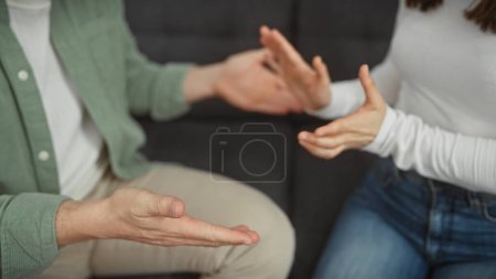 Un hombre y una mujer participan en una discusión con gestos de mano expresivos en la sala de estar de una casa.