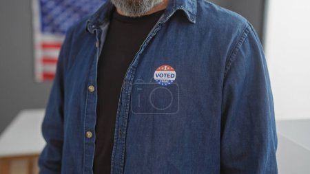 Téléchargez les photos : Gros plan d'un homme barbu portant un autocollant "voté" avec un drapeau américain en arrière-plan symbolisant la démocratie américaine. - en image libre de droit
