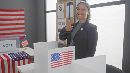 Foto de Mujer sonriente dando pulgares arriba en una cabina de votación con banderas americanas en un centro de votación - Imagen libre de derechos