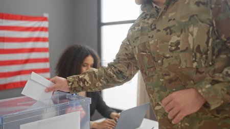 A military man casting a ballot with a focused woman overseeing in a us electoral interior, flag prominent.