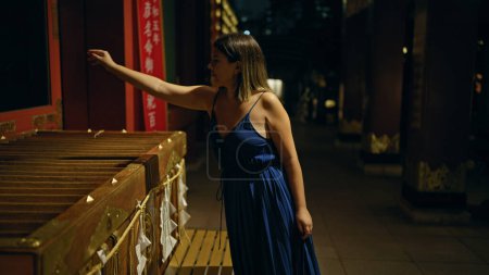 Téléchargez les photos : Belle femme hispanique offrant des pièces en yen dans un temple japonais historique à Tokyo, embrassant l'esprit de la nuit et le culte traditionnel - en image libre de droit