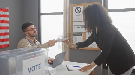 Une femme remet un bulletin de vote à un homme dans un bureau de vote américain avec un drapeau américain en arrière-plan.