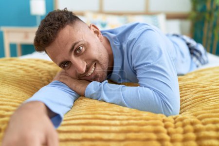 Foto de Joven hombre hispano sonriendo confiado acostado en la cama en el dormitorio - Imagen libre de derechos