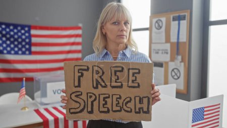 Eine blonde Frau hält ein Schild mit der Aufschrift "Redefreiheit" in einem Wahlzentrum, das mit amerikanischen Flaggen geschmückt ist.