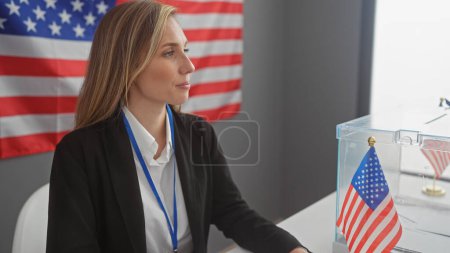 Téléchargez les photos : Une jeune femme blonde dans un cadre professionnel avec un drapeau américain en toile de fond, symbolisant un environnement électoral. - en image libre de droit