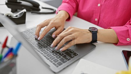 Foto de Una mujer profesional escribiendo en un portátil en una oficina moderna con un reloj inteligente y teléfono en el escritorio. - Imagen libre de derechos