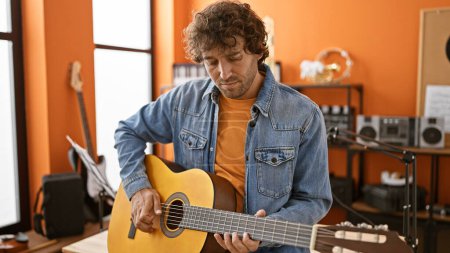 Téléchargez les photos : Bel homme hispanique jouant de la guitare dans un studio de musique, mettant en valeur l'ambiance créative et l'accent artistique. - en image libre de droit