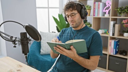 Téléchargez les photos : Homme hispanique avec écouteurs écrit dans un ordinateur portable dans un studio de radio intérieur, exsudant la créativité et la concentration. - en image libre de droit