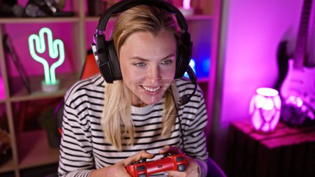 Smiling caucasian woman with headphones playing videogame in colorful gaming room at night