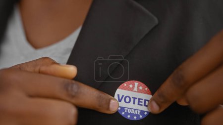 Afroamerikanerin klebt in Innenräumen Aufkleber mit der Aufschrift "Ich habe heute gewählt" an ihren Blazer