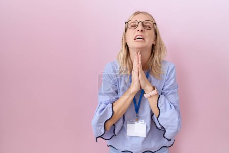 Photo for Young caucasian business woman wearing id card begging and praying with hands together with hope expression on face very emotional and worried. begging. - Royalty Free Image