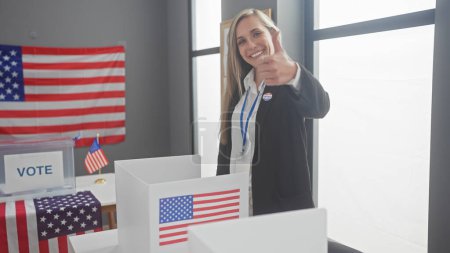 Young blonde woman giving thumbs up inside a voting center with american flags and ballot boxes.