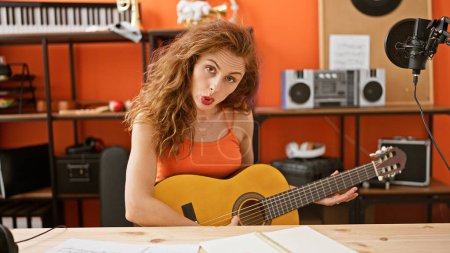 Foto de Una joven caucásica cantando y tocando la guitarra en un estudio de música naranja - Imagen libre de derechos