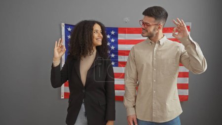 Homme et femme faisant signe "ok" à l'intérieur avec un drapeau américain en toile de fond symbolisant l'affirmation ou l'accord aux Etats-Unis.