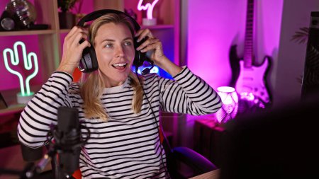 Blonde woman with headphones in neon-lit gaming room smiles engagingly, portraying leisure and technology.