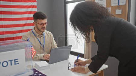 A man and woman participate in the usa electoral process indoors, with american flags, voting booth, and laptop.