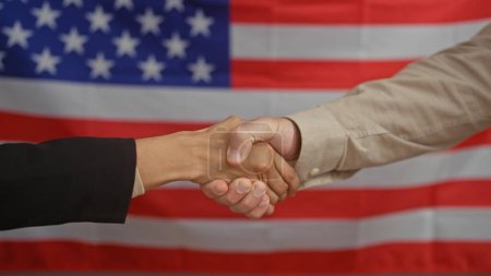 Homme et femme serrant la main dans un bureau avec un drapeau américain en toile de fond, symbolisant la coopération.
