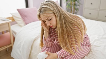 Eine besorgte junge Frau untersucht eine Tablettenflasche, während sie in einem hellen Schlafzimmer auf einem Bett sitzt.