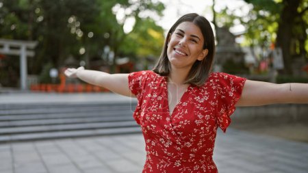 Freudige brünette hispanische Frau, die frei steht, die Arme weit offen in einer lässigen Geste der Umarmung, ihr schönes Lächeln strahlt unbeschwertes Glück im Yasaka-Schrein, Kyoto, Japan aus