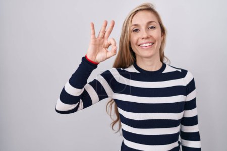 Foto de Mujer caucásica joven con suéter azul marino casual sonriendo positiva haciendo signo de ok con la mano y los dedos. expresión exitosa. - Imagen libre de derechos