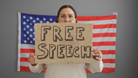 Hispanic woman holding a free speech sign in front of an american flag indoors.