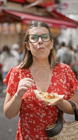 Beautiful hispanic woman snacking on delicious takoyaki balls - a traditional japanese cuisine in the famous dotonbori street's urban city of osaka