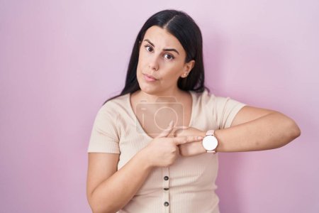 Téléchargez les photos : Young hispanic woman standing over pink background in hurry pointing to watch time, impatience, upset and angry for deadline delay - en image libre de droit