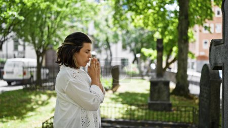 Schöne junge Spanierin betet und trauert am Grabstein auf dem Friedhof