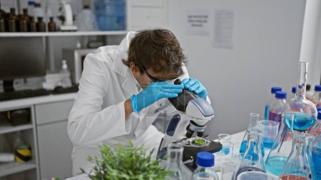 Un homme concentré étudie des échantillons à l'aide d'un microscope dans un laboratoire moderne rempli d'équipements scientifiques et de verrerie.