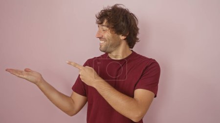 Photo for A smiling hispanic man with a beard presents with his hand against a pink background, conveying a friendly demeanor. - Royalty Free Image