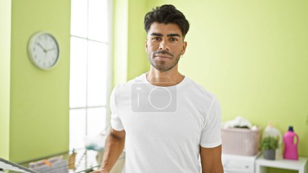Photo for Handsome young adult man with beard standing confidently in a laundry room, looking at the camera. - Royalty Free Image