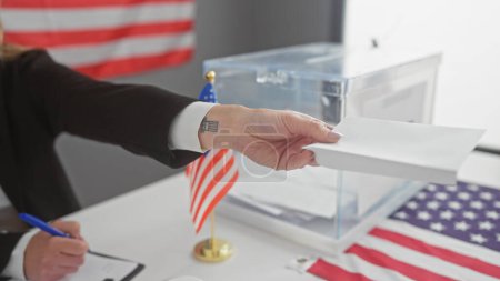 Eine Frau gibt ihren Stimmzettel in einem United States Electory College ab, mit einer amerikanischen Flagge im Blick.