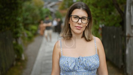 Confident beautiful hispanic woman, sporting glasses and a serious expression, making her stand on kyoto's traditional streets