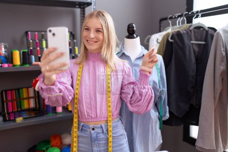 Téléchargez les photos : Jeune femme caucasienne couturière designer sur appel vidéo avec smartphone souriant heureux pointant avec la main et le doigt - en image libre de droit