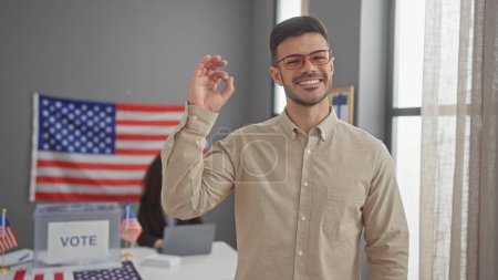 Un hombre sonriente haciendo un gesto bien con una mujer y una bandera de EE.UU. en un telón de fondo del centro de votación.