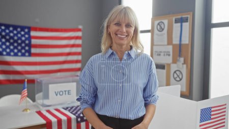 Foto de Una sonriente mujer caucásica en un centro de votación de Estados Unidos con banderas y urnas americanas. - Imagen libre de derechos