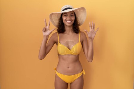 Photo for Young hispanic woman wearing bikini and summer hat showing and pointing up with fingers number eight while smiling confident and happy. - Royalty Free Image