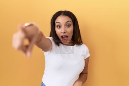 Téléchargez les photos : Jeune femme arabe portant un t-shirt blanc décontracté sur fond jaune pointant du doigt surpris devant, bouche ouverte expression étonnée, quelque chose sur le devant - en image libre de droit