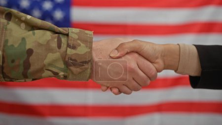 Eine zivile Frau und ein militärischer Mann geben sich vor einer amerikanischen Flagge die Hand und symbolisieren damit die Kollaboration.