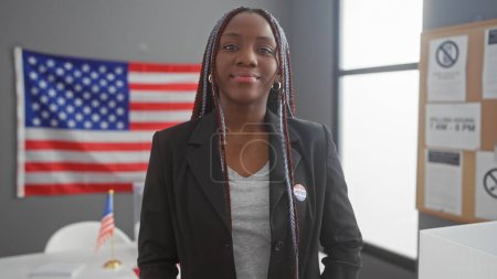 Photo for Confident african american woman with braids wearing an 'i voted' sticker in a room with american flag - Royalty Free Image