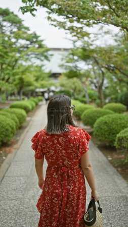 Im Herzen Tokyos geht eine schöne hispanische Frau mit Brille lässig rückwärts vom berühmten Glückstempel gotokuji weg und hinterlässt eine auffällige Rückansicht ihrer brünetten Haare